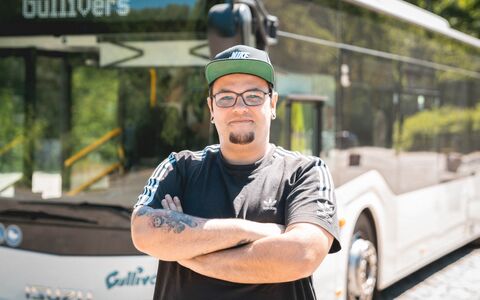 Ein junger freundlciher Busfahrer steht vor seinem Linienbus
